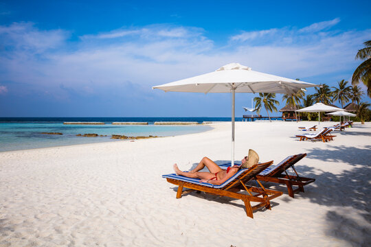 Woman relaxing on lounge chair at the beach, Maldives