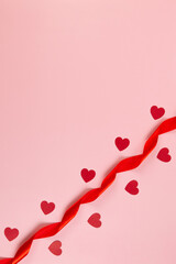 Top view of red ribbon and red hearts on pink background. Valentine's day, love. Shiny rolled fabric, silk and satin material. Copy space, flat lay.