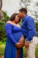 Obraz premium Loving hispanic husband kissing pregnant wife's forehead in park