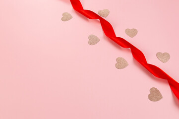 Top view of red ribbon and pink glitter hearts on pink background. Valentine's day, love. Shiny rolled fabric, silk and satin material. Copy space, flat lay.