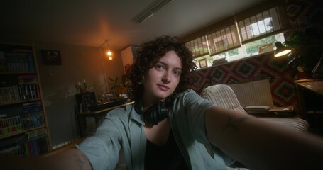 A young woman smiles looking at the camera as if she is taking selfie on a mobile phone. She's...