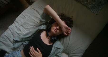 Upset young woman looks at the camera lying on the bed, top view