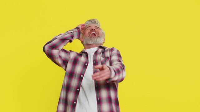 Caucasian amazed middle-aged mature man on yellow background with explosive surprise loud shout turning into contagious laughter. Abrupt shift from shock to happiness capturing intense comedic emotion
