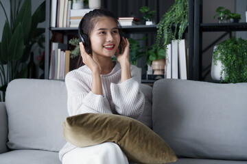 Asian woman sits on sofa listening to music in living room