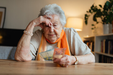 Elderly woman looking sadly at few banknotes in her hand. Concept of financial concerns for seniors.