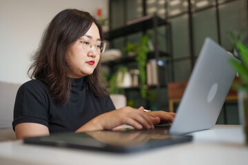 Fototapeta premium concentrated Asian woman using laptop computer creative girl working and typing on keyboard
