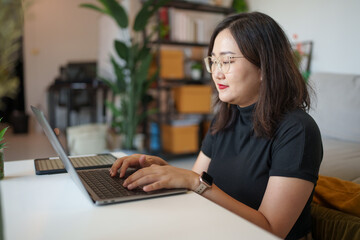 concentrated Asian woman using laptop computer creative girl working and typing on keyboard