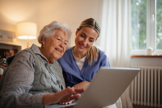 Social worker helping elderly lady with managing her finances, teaching her to use laptop.