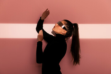 Woman wearing futuristic glasses and gesturing against pink background