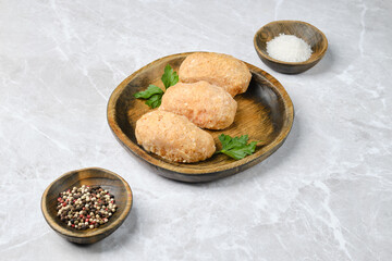 Three chicken semi-finished cutlets on a wooden plate garnished with fresh parsley