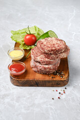 Freshly prepared meat patties with condiments on a wooden board in a bright kitchen