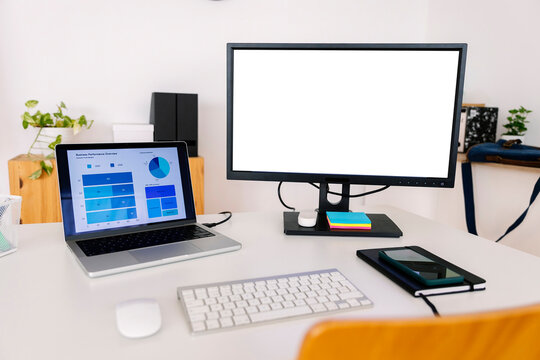 Laptop with charts and graphs near desktop PC on desk in office