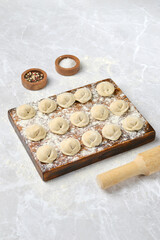 Dough dumplings ready for cooking on a wooden board amid flour and spices