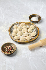 Freshly made dumplings arranged on a wooden plate with spices and rolling pin on a marble surface