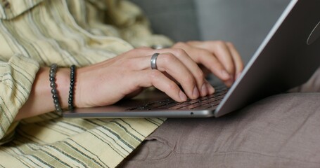 Obraz premium A man is typing on a laptop keyboard, holding it on his lap. Close-up of his hands, an unrecognizable person