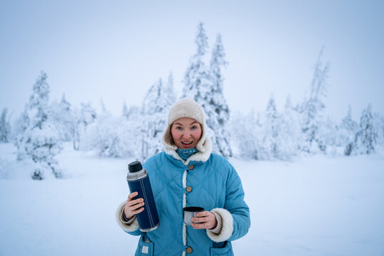 Woman pouring a hot drink from a thermos into a cup in winter forest