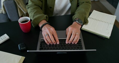 A man typing on a laptop keyboard sitting at his desk. Close-up of his hands, an unrecognizable...