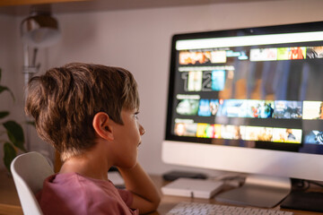 Elementary school student watching educational videos on streaming platform using desktop computer at home, enjoying online learning experience and expanding knowledge