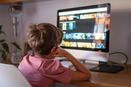 Young boy sitting at desk watching educational videos on streaming platform using desktop computer at home, engaging with online learning resources