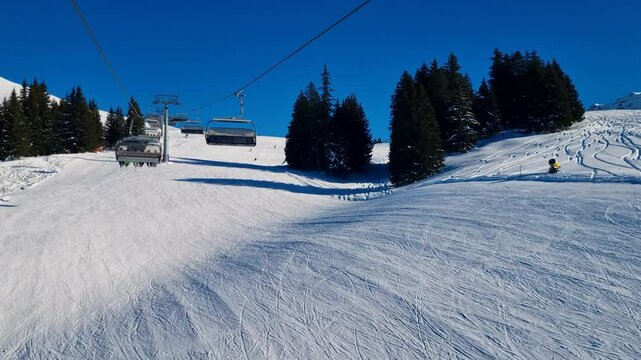 Chairlift shot in the Adelboden-Lenk ski area, transporting tourists on top of B&uuml;hlberg mountain. Skiers glide down powdery slopes on a sunny day under a clear blue sky
