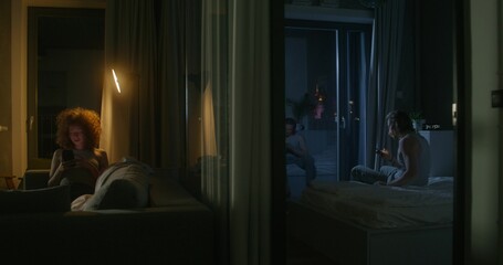 A man and a woman use mobile phones at night. They are sitting in different rooms. Online correspondence. Insomnia