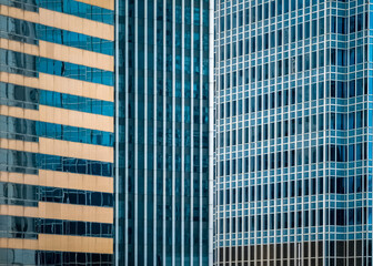 Close-up view of several skyscrapers in Hong Kong, showcasing the architectural details and patterns of their glass facades.  Different shades of blue and beige create a striking contrast.