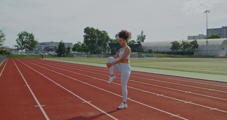 A woman in sports clothes does exercises standing at the city stadium on a summer day