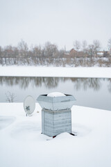 A massive satellite dish is perched on an icy snowy roof, surrounded by frozen streams,...