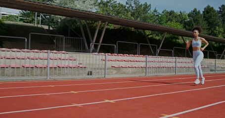 A woman in sports clothes and with earphones in her ears runs at the stadium on a summer day