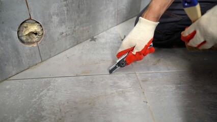 Construction worker cutting grout lines on floor tiles with utility knife