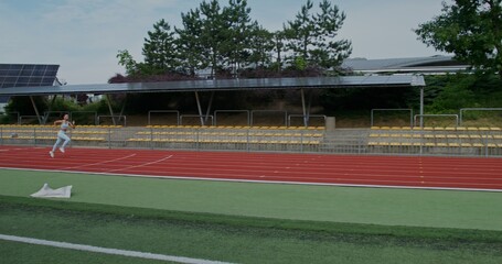 Obraz premium A woman in sports clothes runs at speed in the stadium, side view. Summer day