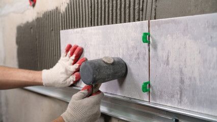 Construction worker installing large format tile with rubber mallet and leveling system