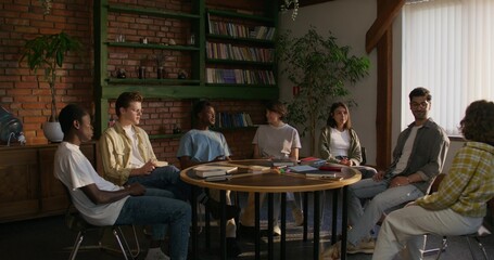 Bible Study Group. Young people talk in pairs while sitting at a table indoors. The books are on the table. Daylight
