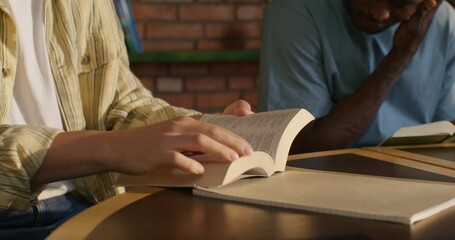A man opens his Bible while sitting at a table indoors. Close-up of his hands, an unrecognizable person