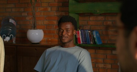A man is smiling and talking to his friends while sitting at a table indoors. Daylight