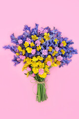 Bunch of Spring wildflowers on pink background with bluebell, buttercup and red campion flowers. Nature floral bouquet arrangement. Symbol of Beltane festival