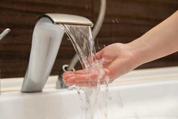 Woman touches flowing water from tap into bathtub in bathroom with hand.