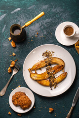 Bananas flambe on a white plate with nuts and chocolate on a table with coffee and a cezve on a dark background with a knife and fork. Top view. Restaurant serving dessert