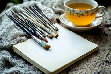 Artistic Workspace with Paintbrushes, Sketchbook, and Cup of Tea