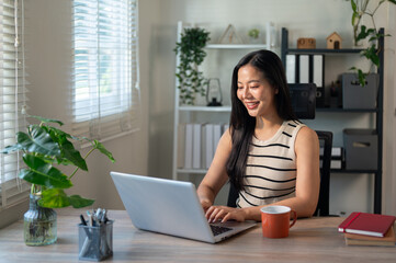 An attractive Asian businesswoman in casual clothes is working on her laptop in her office.