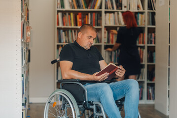 Man in wheelchair reading a book in library while librarian searching for a book