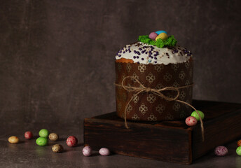 Easter cupcake with icing on wooden box on dark background with colored eggs