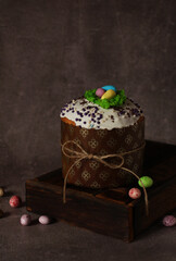 Easter cupcake with icing on wooden box on dark background with colored eggs