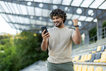 Man in stadium holding phone in hands, satisfied with training results, holding hand up...