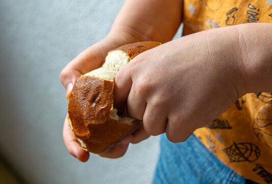 a child holding a dry kaiser roll in his hands. a little boy chomping and eating the middle of a roll.