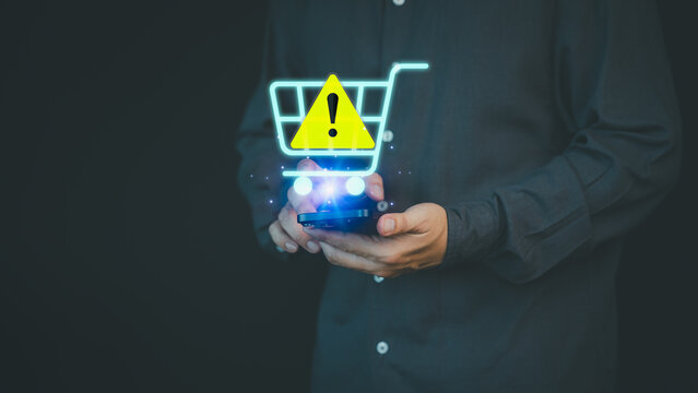 Male customer use smartphone with caution warning sign on shopping cart for notification error of online shopping. Business technology concept of warn and danger sign, scam and theft in cybersecurity.