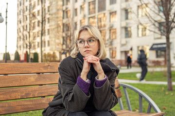 Fototapeta premium A woman sits contemplatively on a bench outside. Woman in the city.