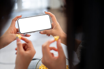 Two female friends chatting and snacking while watching a movie on a phone together on a sofa.