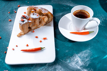 Tarte Tatin a French banana dessert, a slice of pie on a white plate with freeze-dried raspberries and hot chili peppers with a cup of strong coffee on a dark green background. Space for text,
