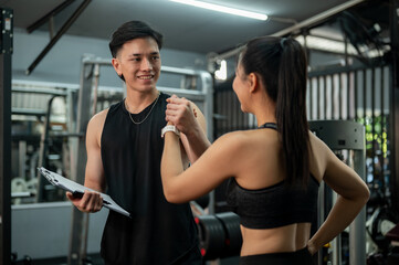 Fototapeta premium A cheerful Asian male fitness instructor is holding a client hand to cheer up after discussing.